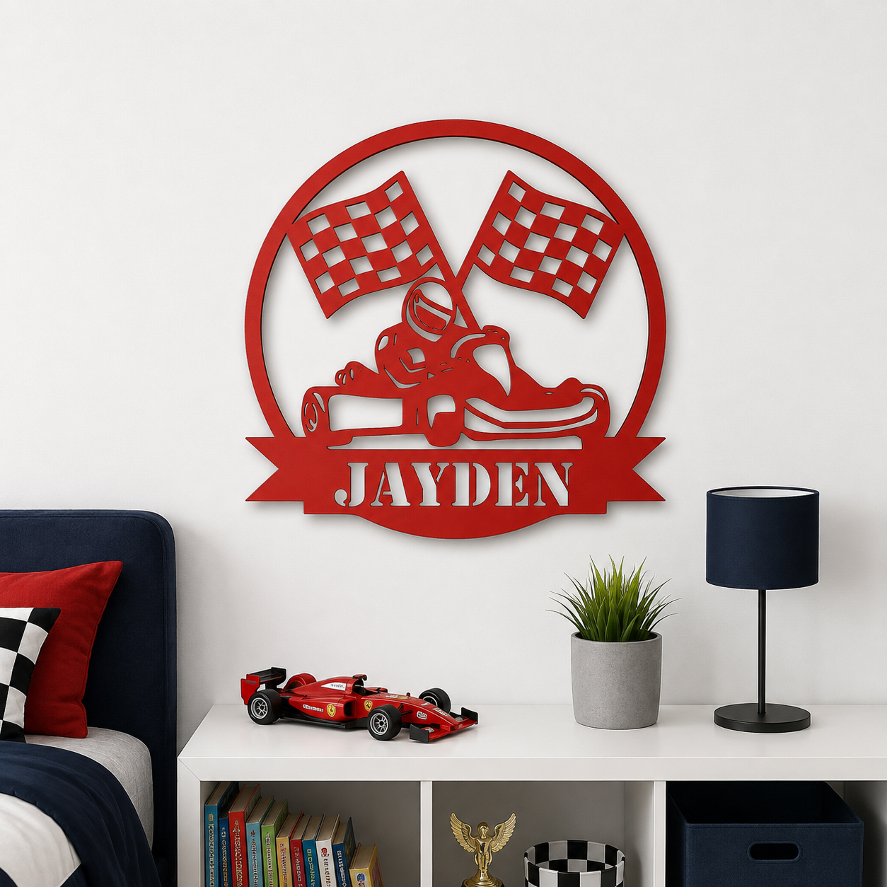 A red metal wall art piece featuring a go-kart, checkered flags, and the name 'JAYDEN' in a circular frame, displayed on a white wall above a shelf with a toy race car, books, and a lamp.